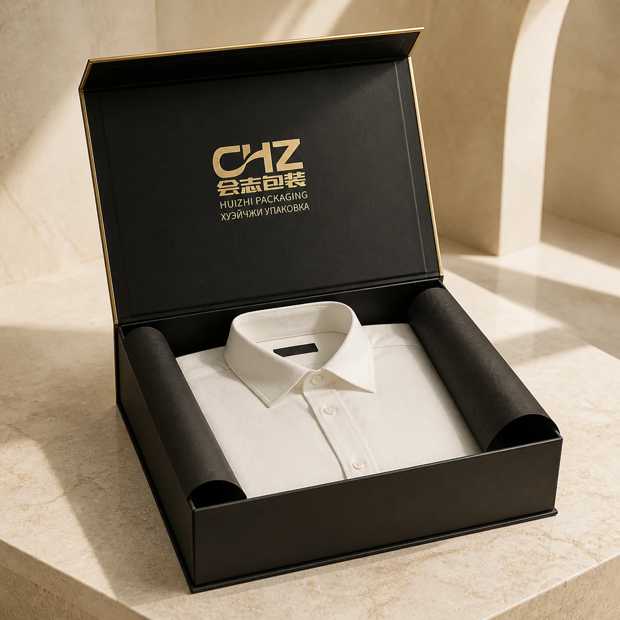 Open matte black magnetic rigid box with gold edging holding a folded white dress shirt between black tissue rolls.