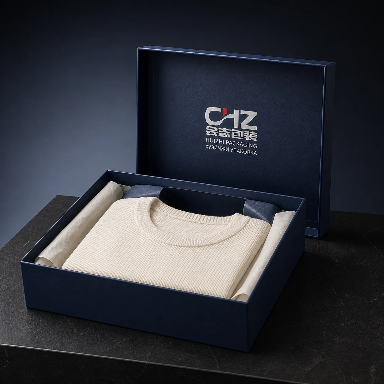 Open deep navy lift-off lid-and-base box presenting a folded ivory knit sweater between tissue-lined sides.