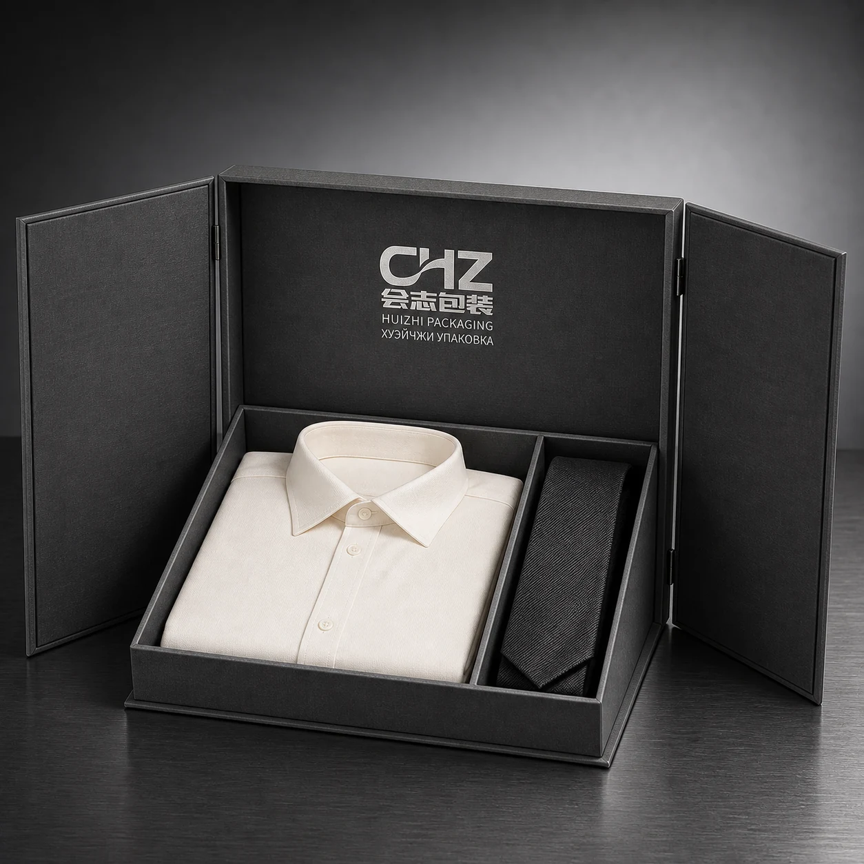 Open charcoal double-door rigid box with separate compartments for a folded white shirt and black tie.