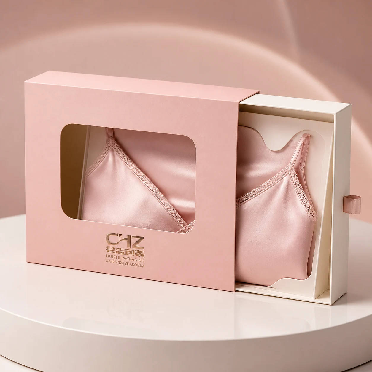 Blush pink sleeve-and-drawer lingerie box with a die-cut window revealing a neatly arranged pale rose camisole.