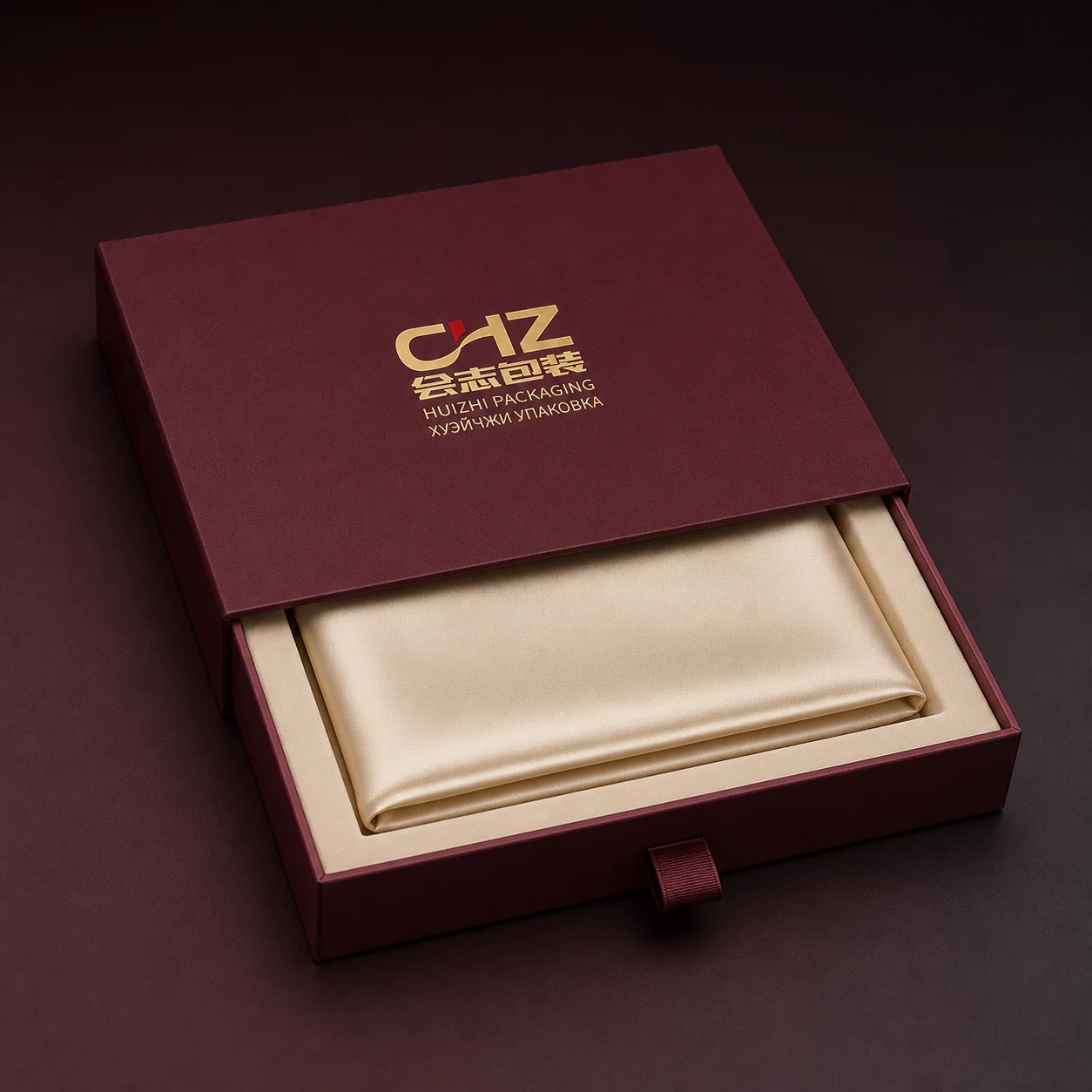 Open burgundy rigid drawer box presenting a folded scarf in a fitted shallow tray.