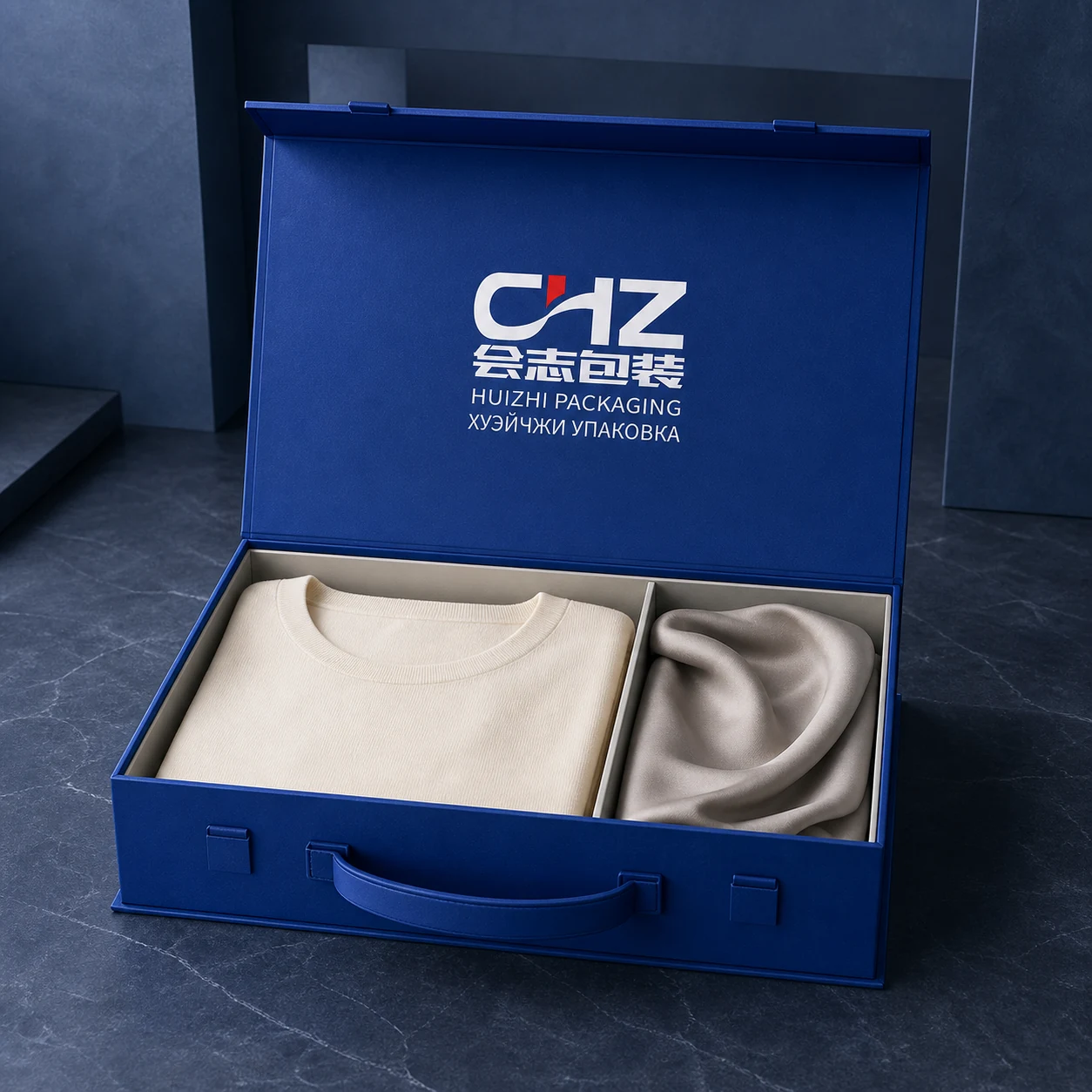 Cobalt blue rigid fashion set box with a carry handle presenting folded apparel and coordinated accessories.