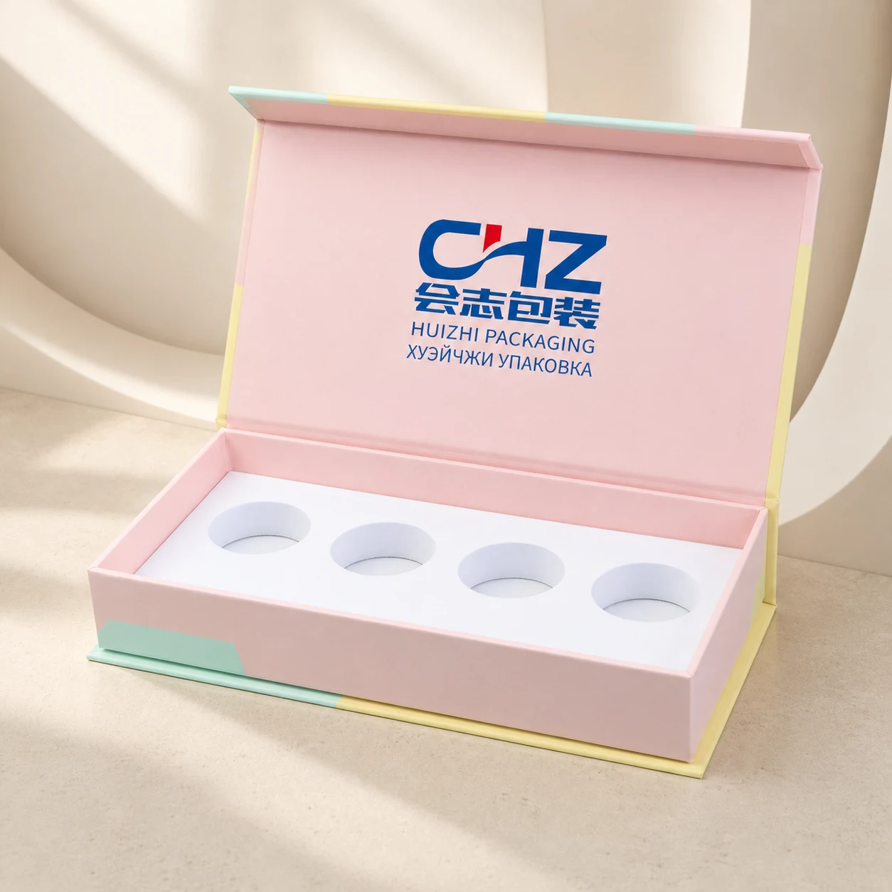 Open pastel pink magnetic rigid cosmetic box with four circular insert cavities on a warm ivory architectural background.
