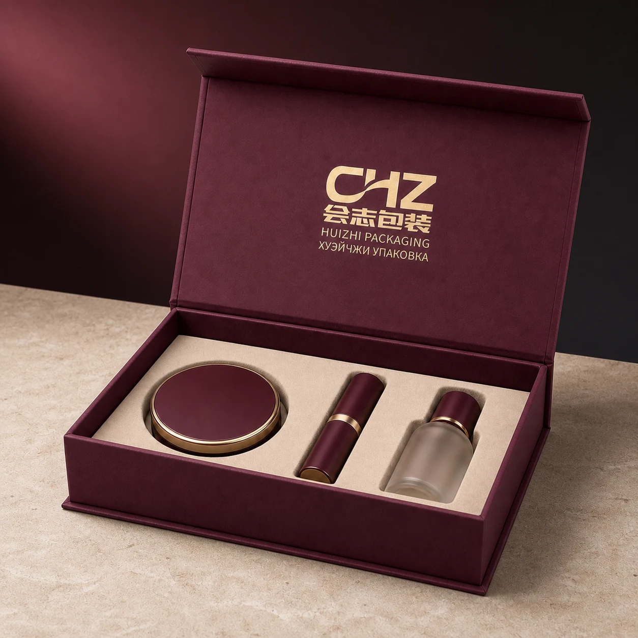 Open burgundy rigid makeup gift box holding a compact, lipstick tube, and frosted bottle in an ivory insert.