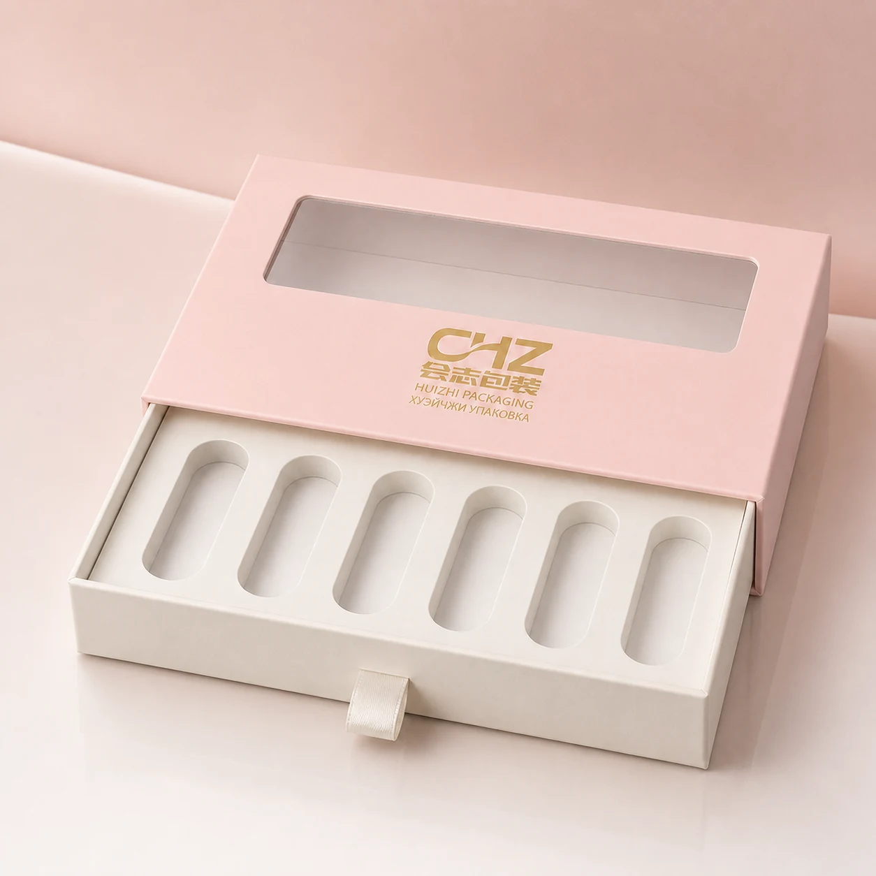 Blush pink windowed cosmetic sleeve with an ivory pull-out drawer and six empty long product slots on a pearl white surface.