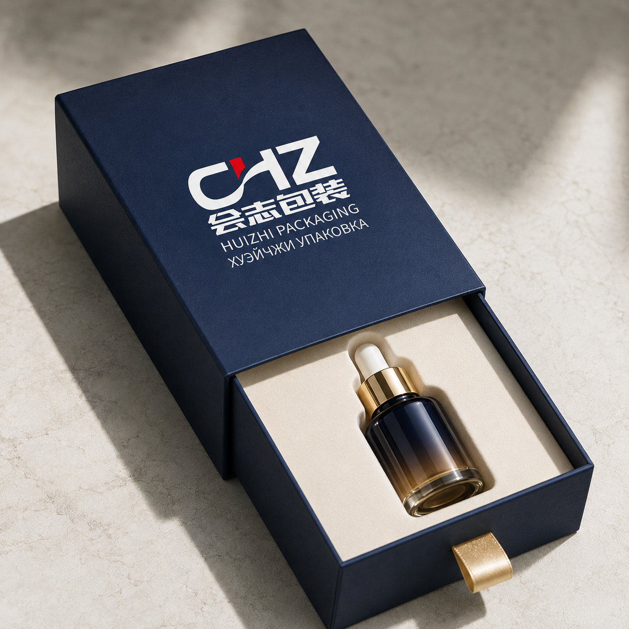 Open navy rigid drawer box with Huizhi Packaging branding, gold ribbon pull, cream insert, and skincare serum bottle.