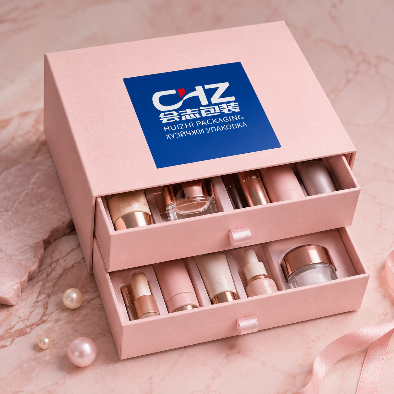 Blush pink double-drawer rigid box with Huizhi Packaging branding and two open trays filled with beauty products.