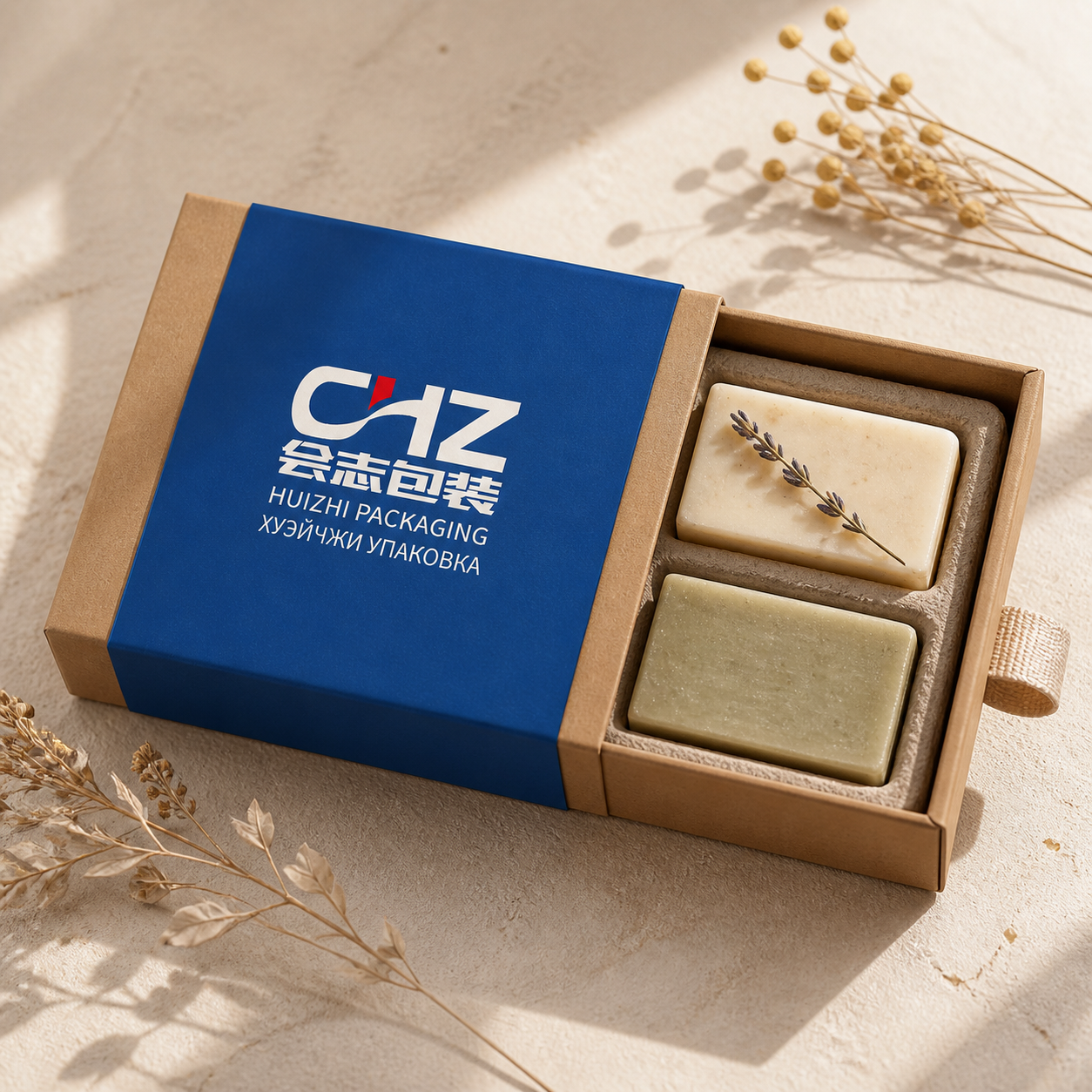 Open kraft drawer box with blue Huizhi Packaging sleeve and two handmade soap bars in a divided fiber insert.