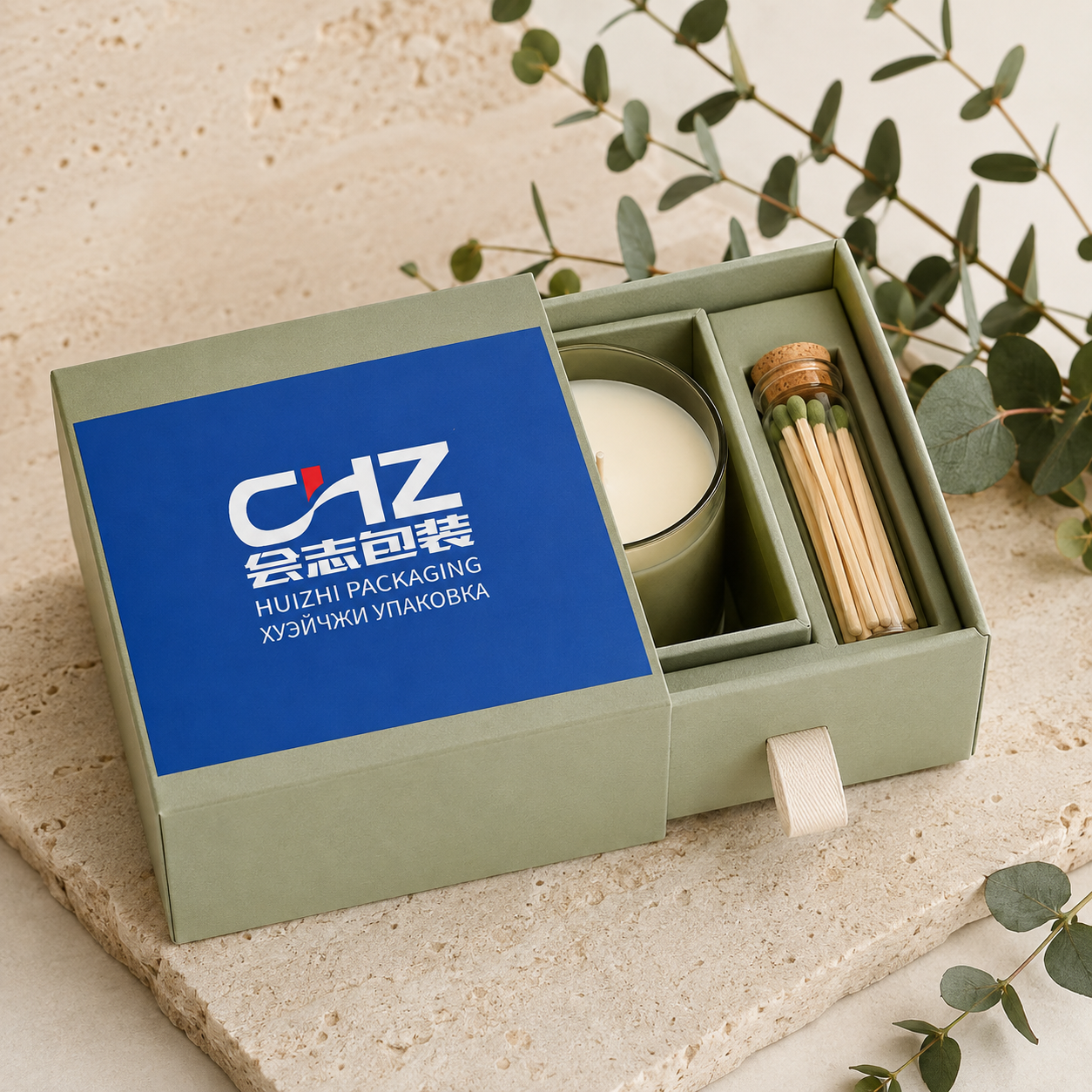 Open sage green drawer box with blue Huizhi Packaging sleeve, candle, match bottle, and divided insert.