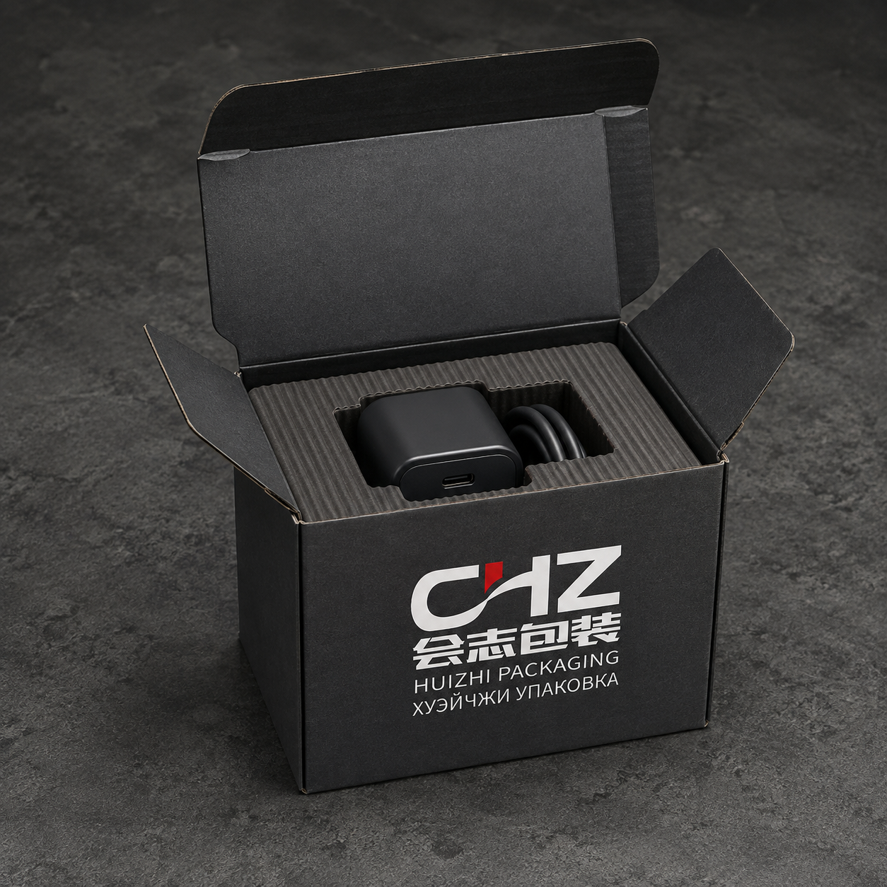 Open charcoal folding carton with Huizhi Packaging logo and corrugated insert holding a compact charger and cable.
