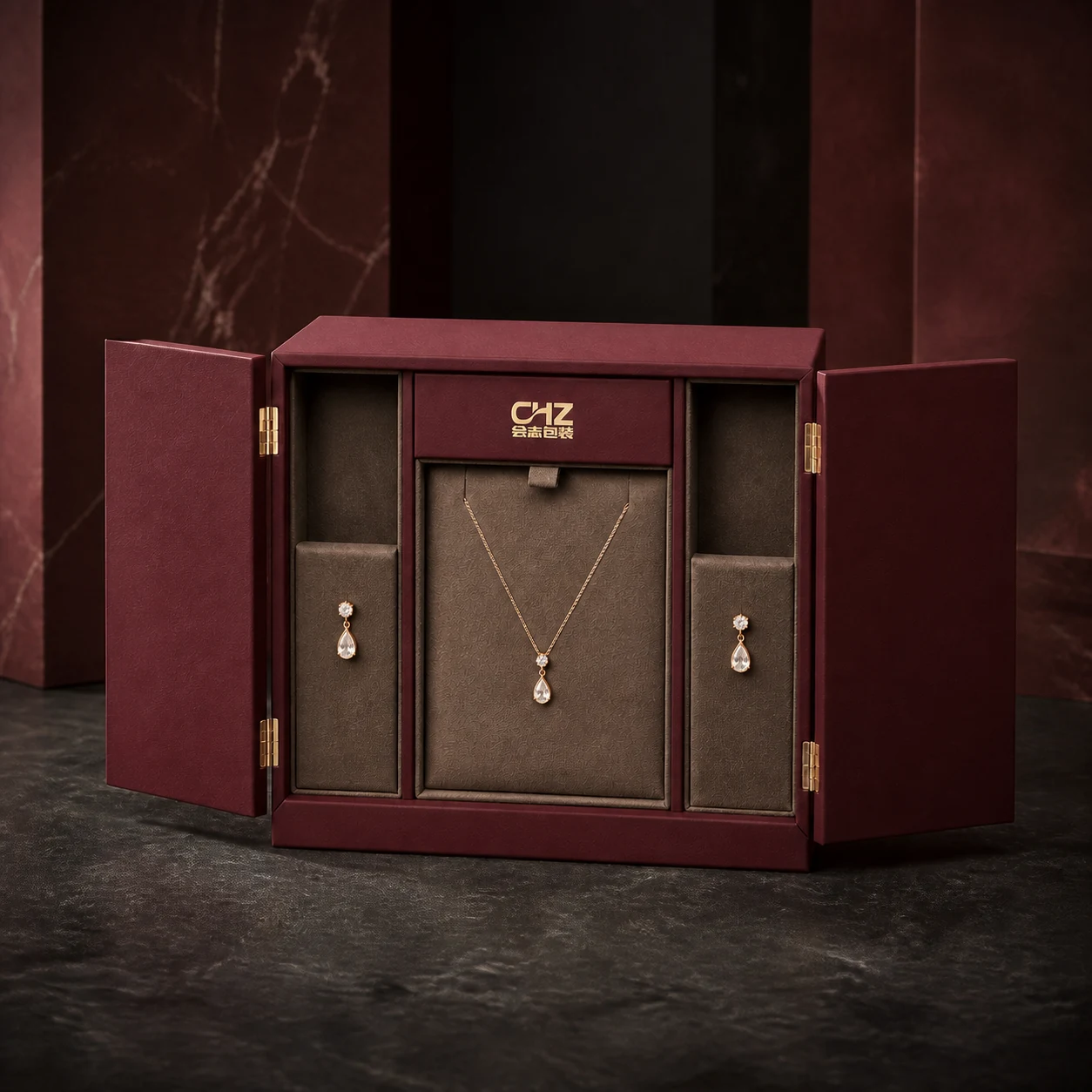 Open burgundy double-door rigid jewelry box with a necklace in the center and earring compartments on both sides.