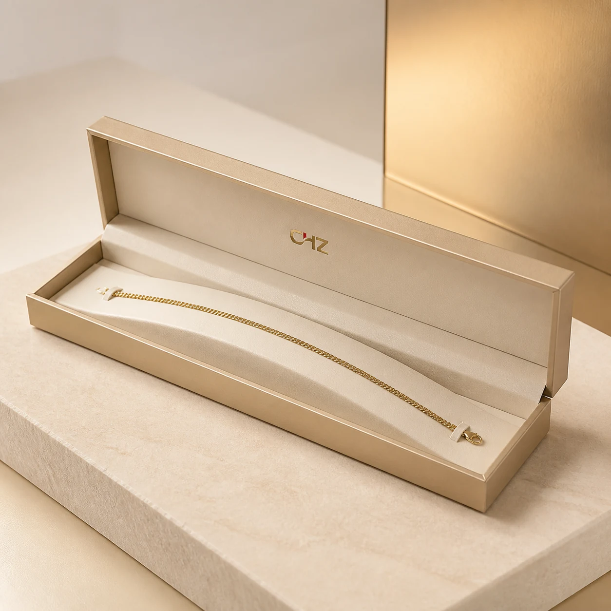 Open champagne-colored long hinged bracelet box presenting one unbranded chain bracelet on a curved ivory support.